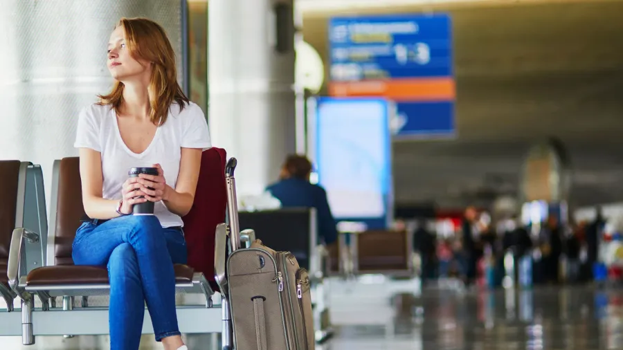 young woman in international airport with luggage and coffee to