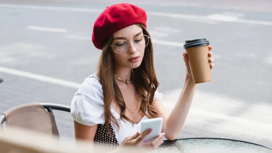 young woman in red beret and eyeglasses holding paper cup