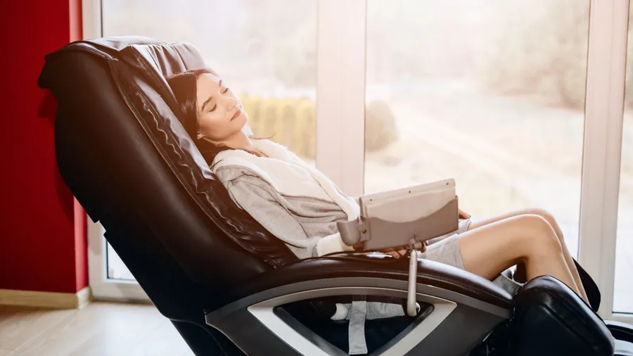 A woman relaxing on a massage chair near the window.