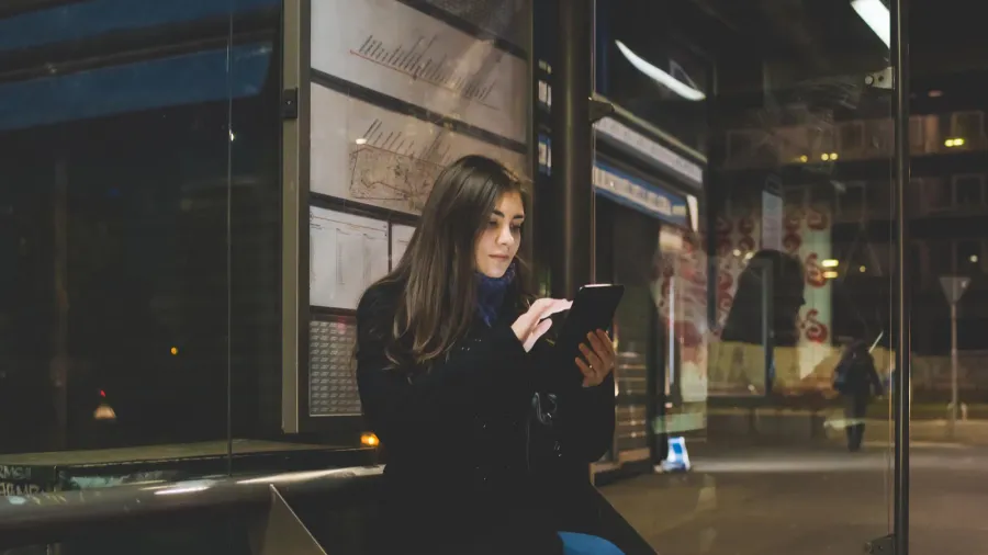 young woman sitting bus stop using smartphone  technology phubber