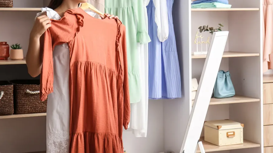 young woman trying on stylish dress near mirror in walkin