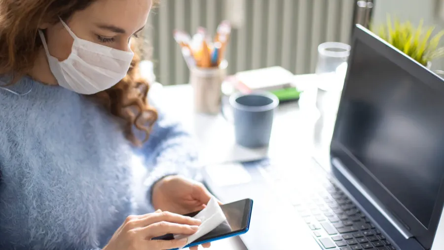 young woman wiping smartphone with disinfectant wipe while working from