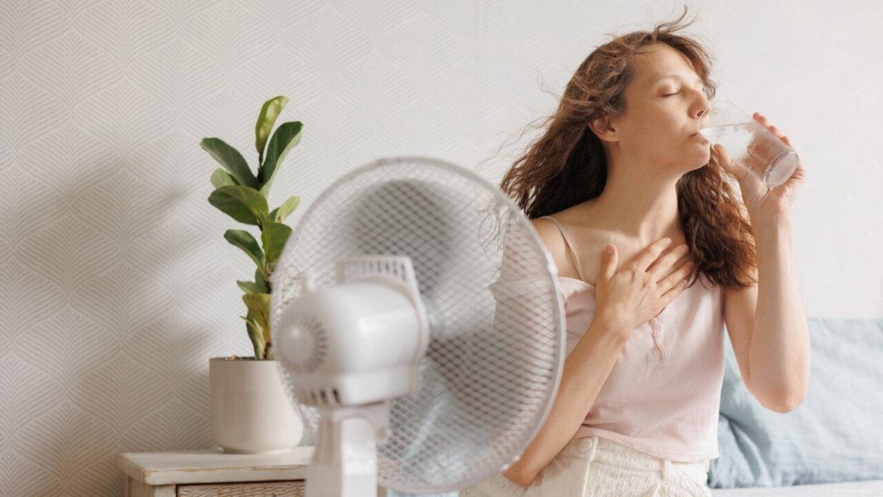 A girl smiling and feeling the refreshing breeze from a fan on a hot summer day