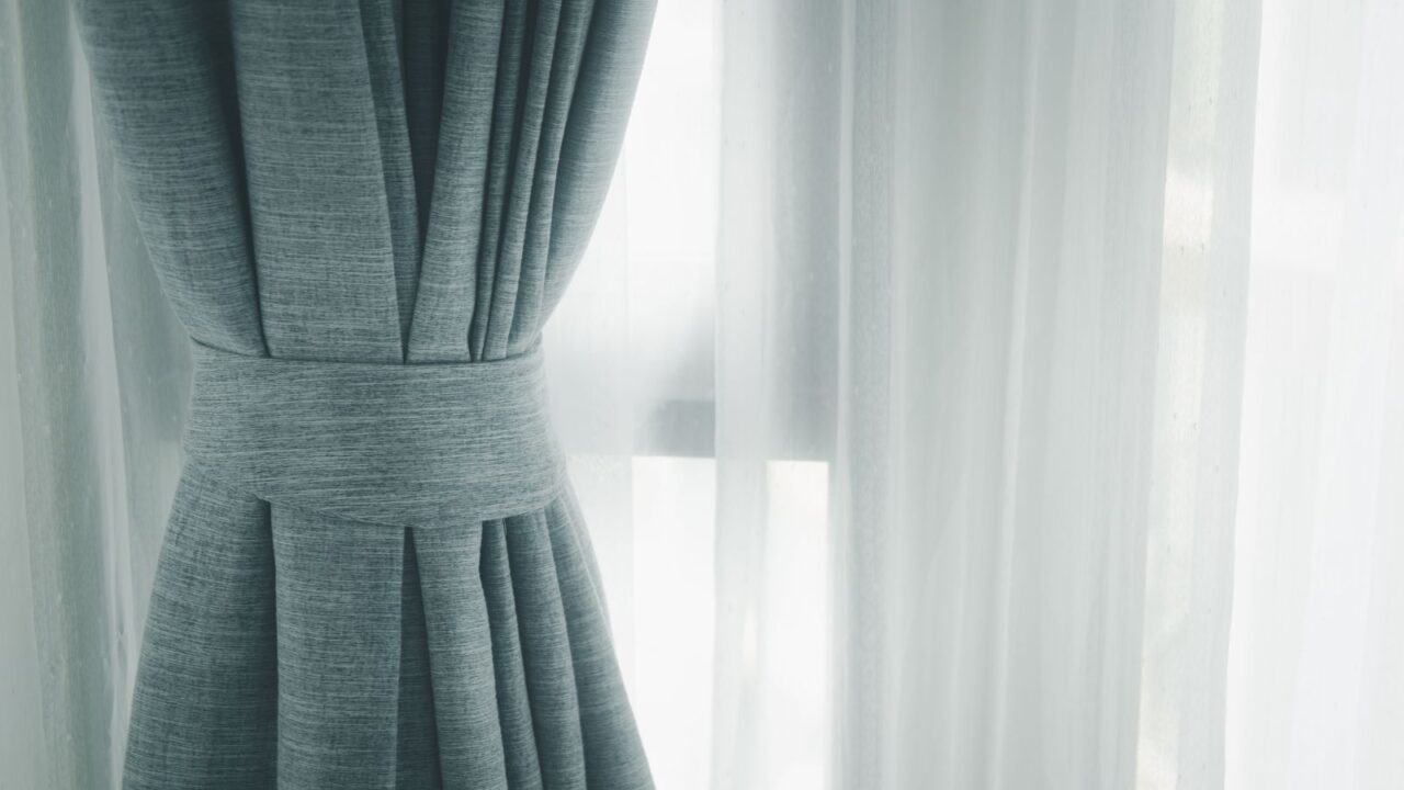 A window with sheer curtains and a layer of heavy gray drapes in front of them.