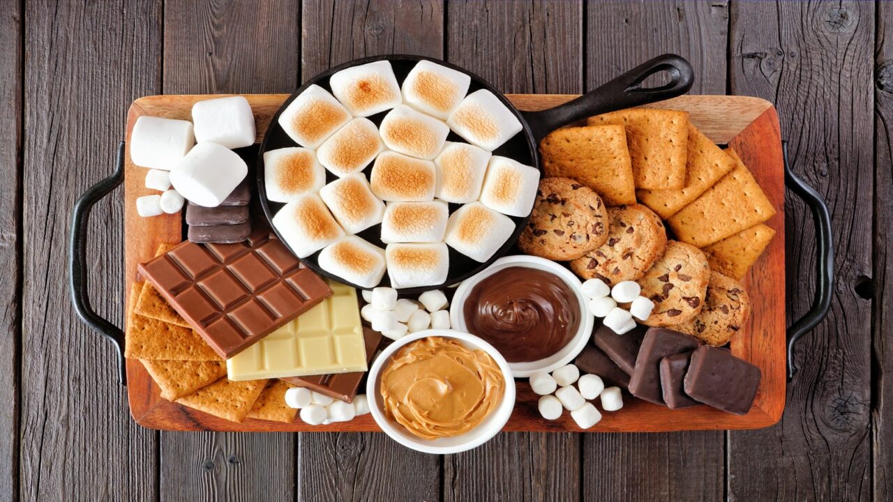 A s'mores bar tray with roasted marshmallows, crackers, chocolate bar, and cookies.