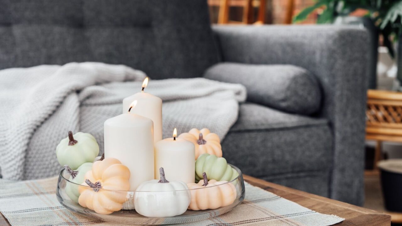 A glass dish filled with neutral color pumpkins and white candles.