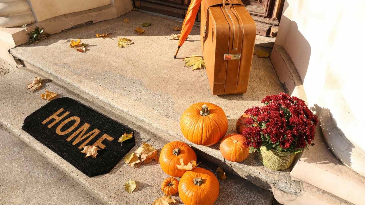 Decorated doorstep with pumpkins, umbrella and a mat with some fall leaves scattered on the ground