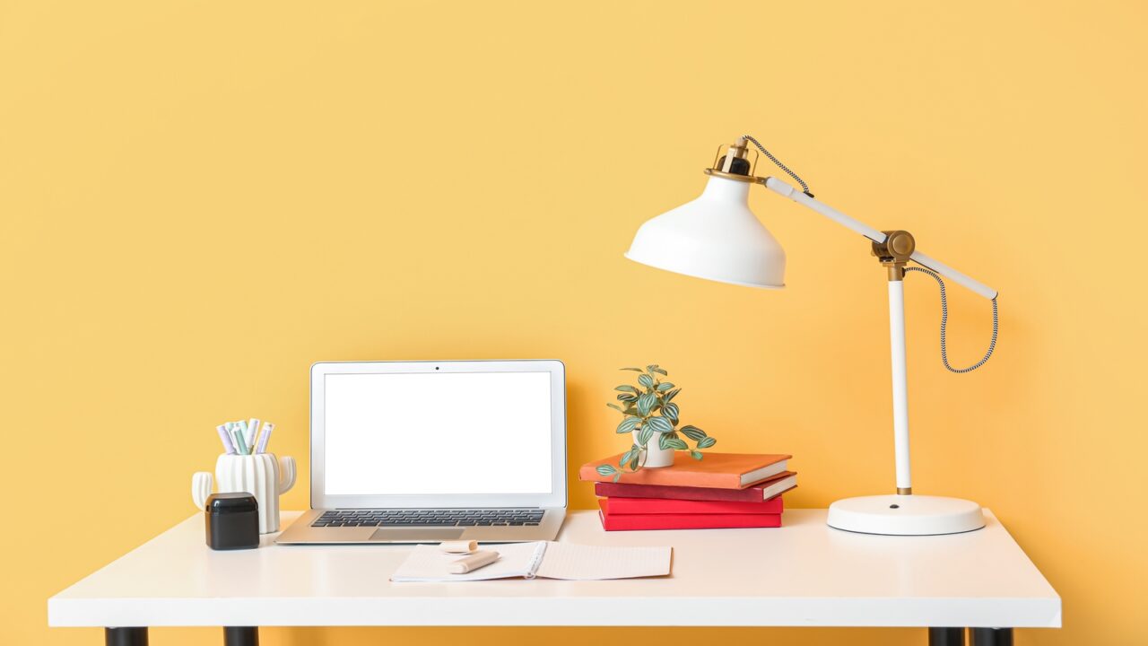 An office desk with essentials like a laptop, desk lamp, books, pencil holder etc.