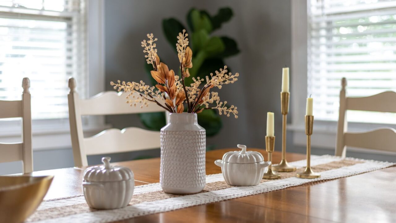 A vase with fall flowers with pumpkin decorative items and candles