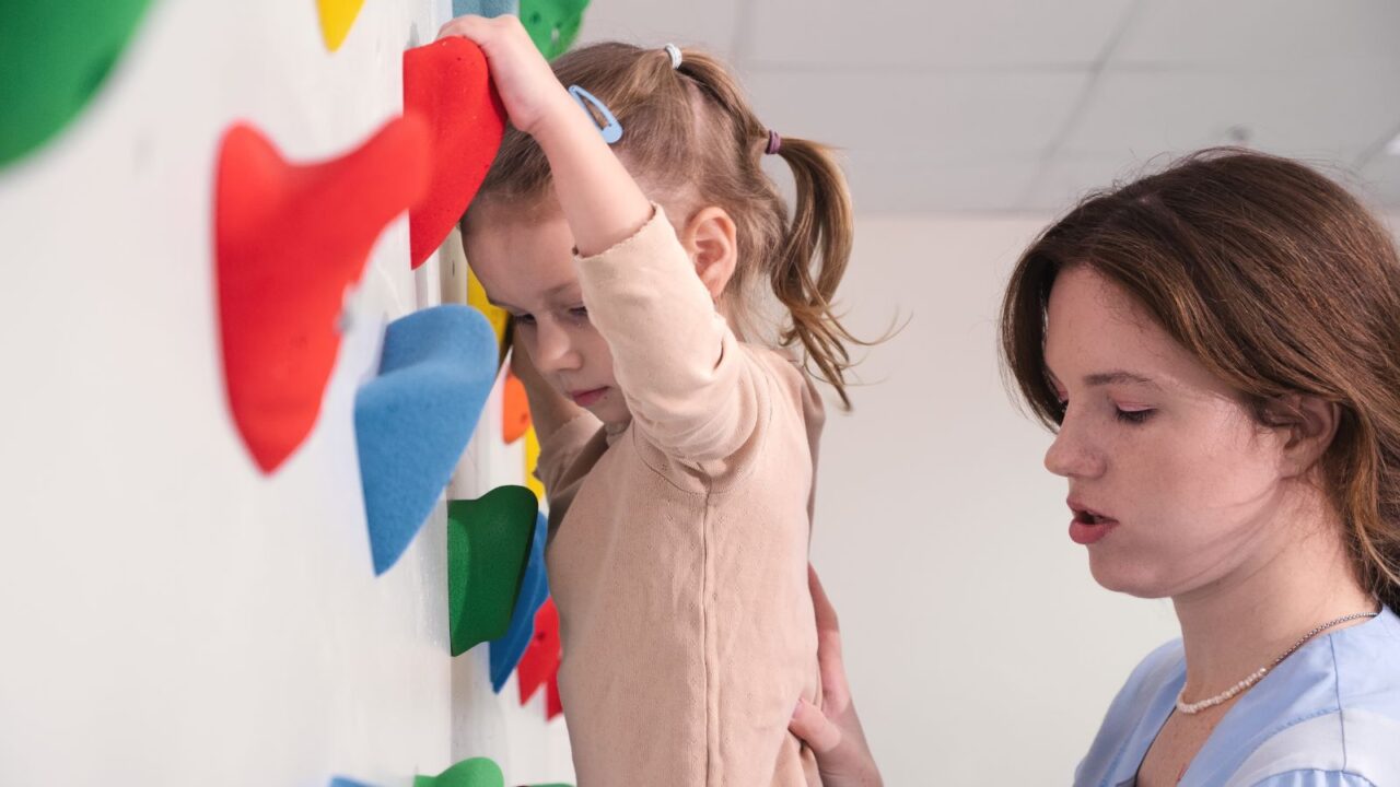 A woman helping a child climb a wall