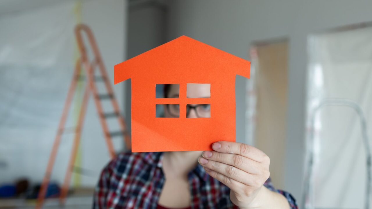 A person proudly holding an orange houseshaped cutout in their hands, symbolizing creativity in home renovation