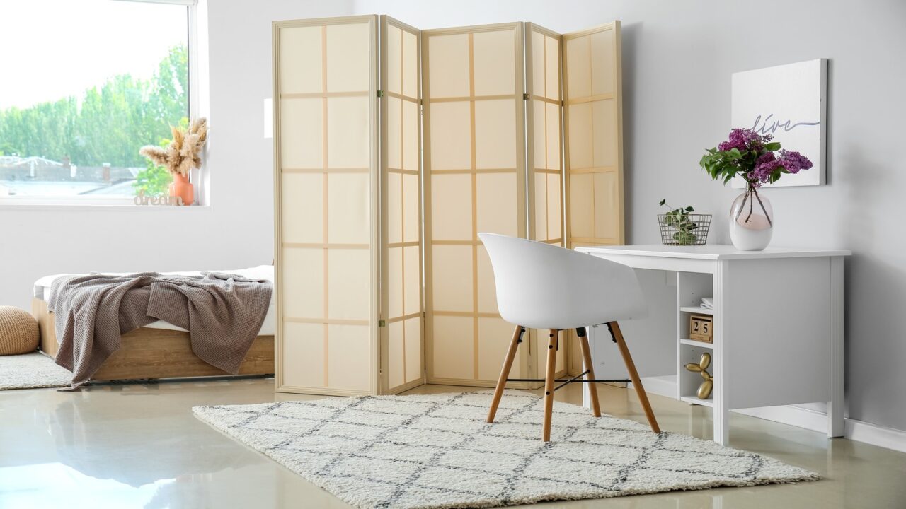 A workspace in a bedroom with white gloss-finish table and white chair on a rug.
