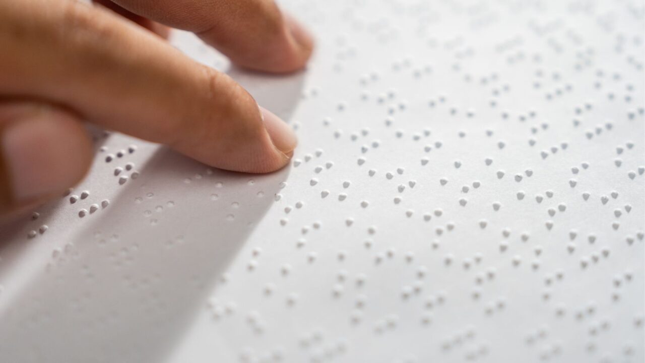 Hand of a blind person reading some braille text on page paper to learn.