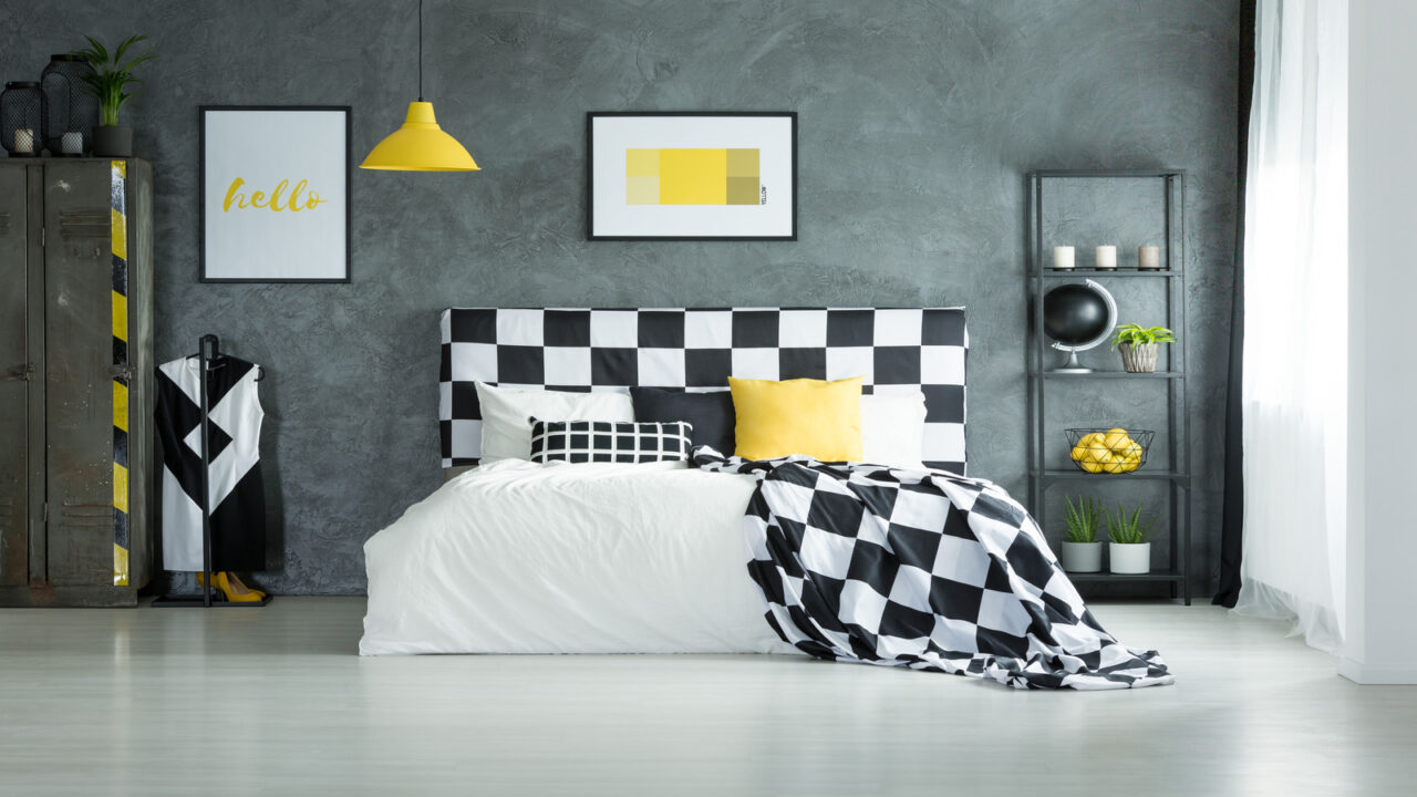 A cozy bed and shelf with decor accents in front of a industrial gray accent wall with artwork in a bedroom.