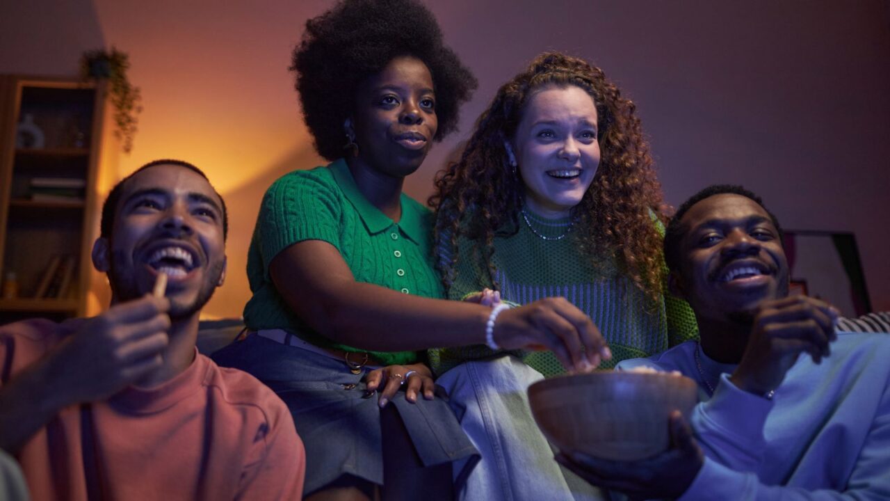 Multiethnic group of excited young people watching TV together in a dark room