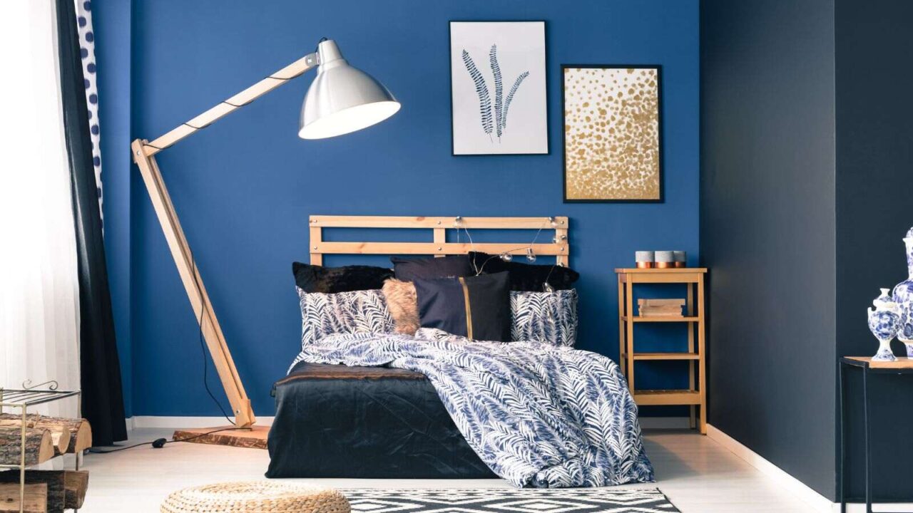 Navy and dark blue bedroom with wooden bed, floor lamp, and framed artwork hanging on the wall.