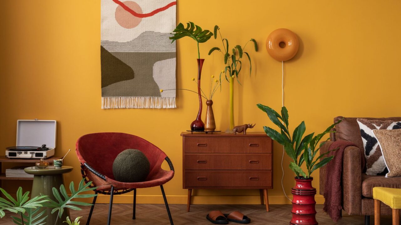 living room with a yellow wall, featuring a red armchair, a vintage dresser, and various plants.