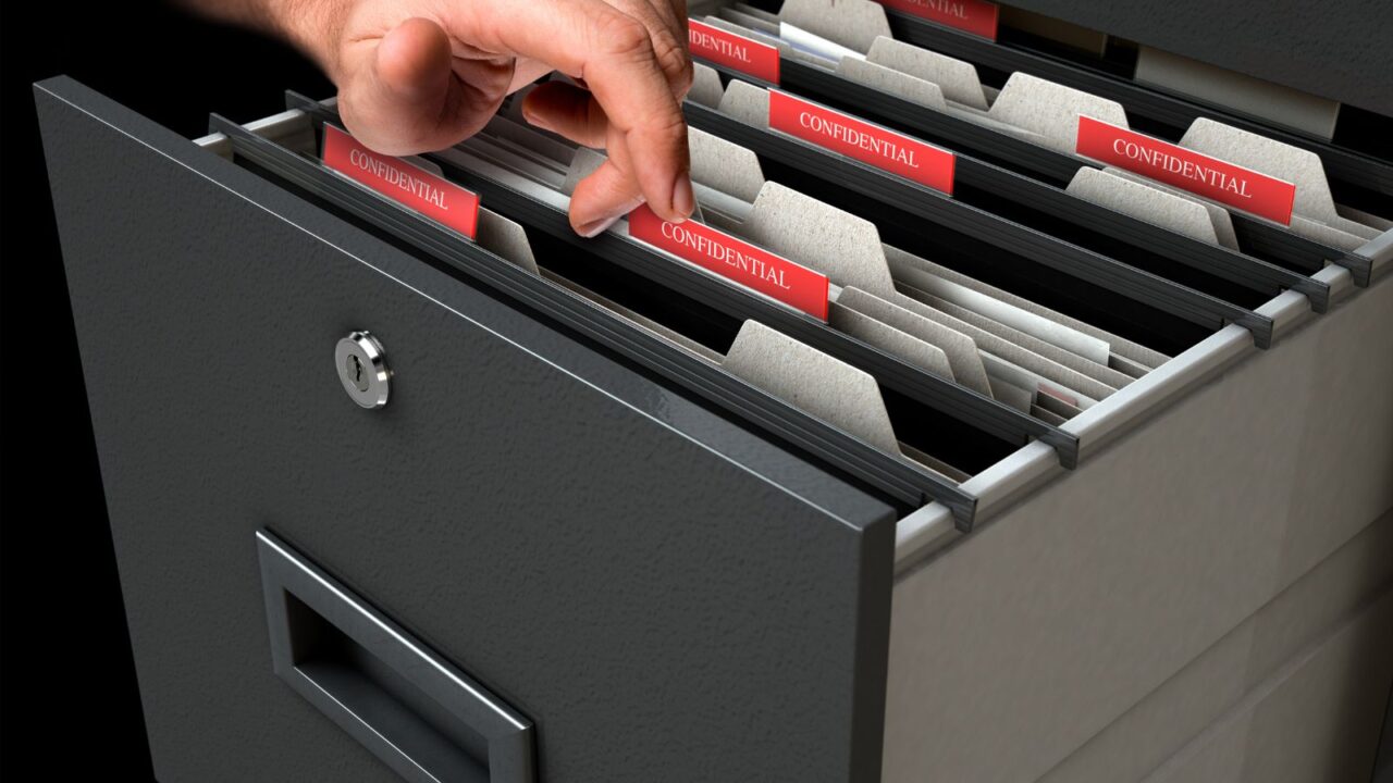 A male hand searching through confidential related documents in a filing cabinet drawer