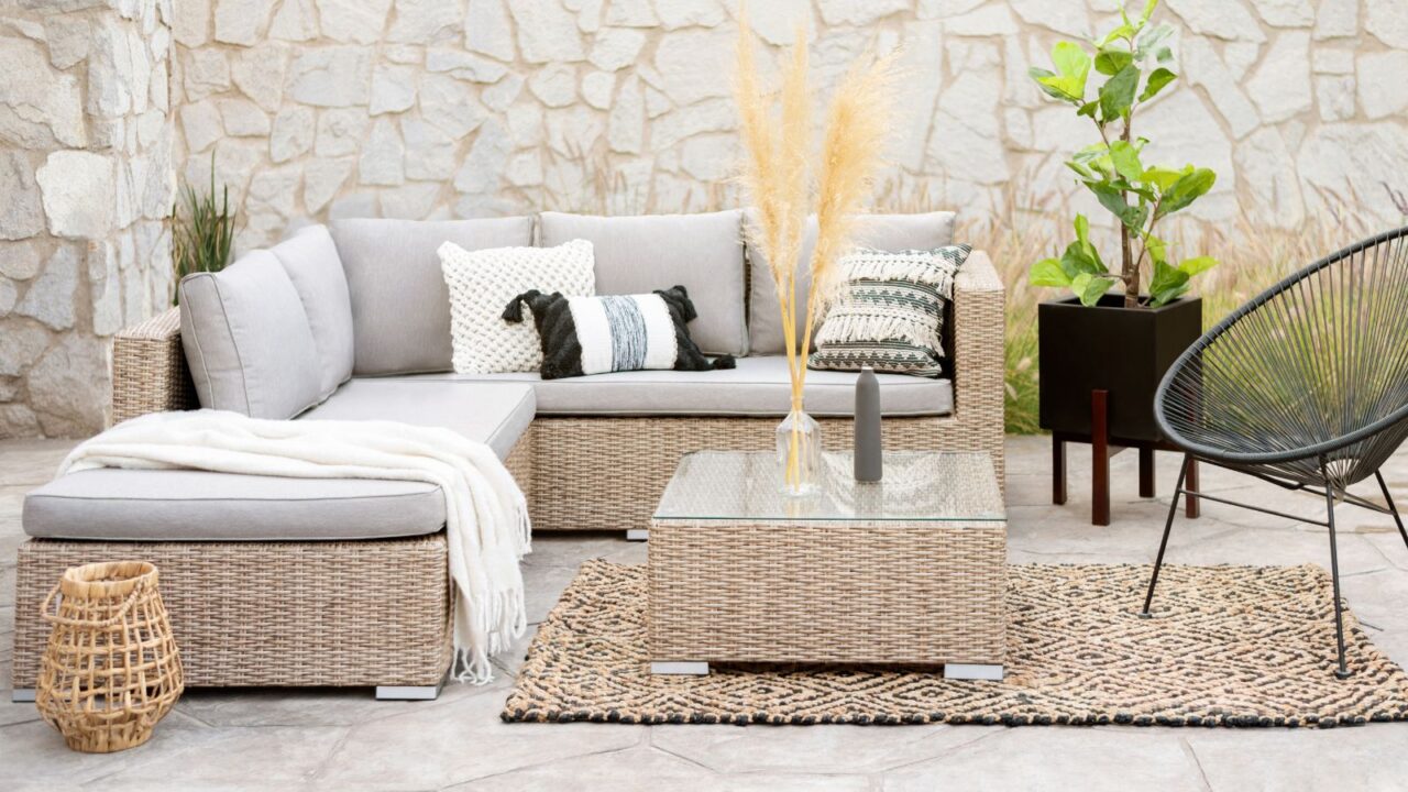 A matching furniture set on a patio with rattan sectional sofa, decorative pillow covers, rattan coffee table, and rug.