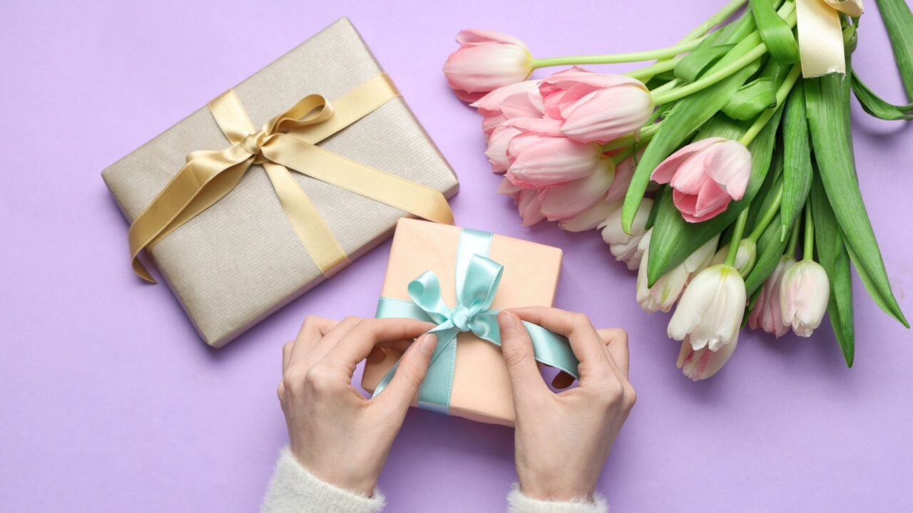 Female hands with gift boxes and bouquet of beautiful tulips on purple background.