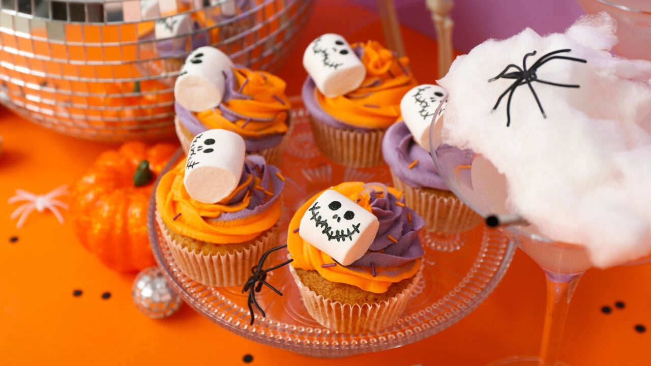 Halloween cupcakes decorated with spooky marshmallows on orange table, closeup