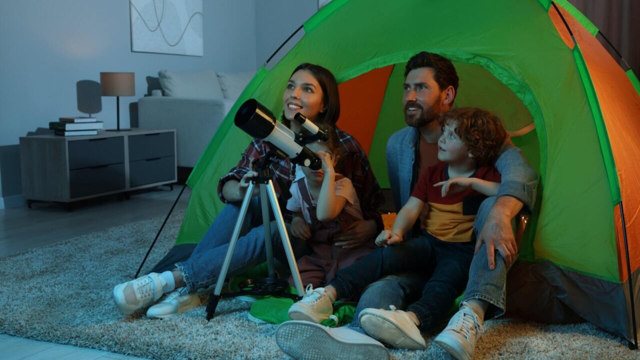 Happy family watching stars using telescope indoors in a camp