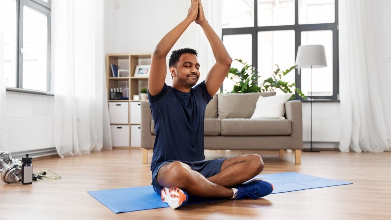 A young man sitting on a yoga mat in lotus yoga pose in a Zen-inspired room