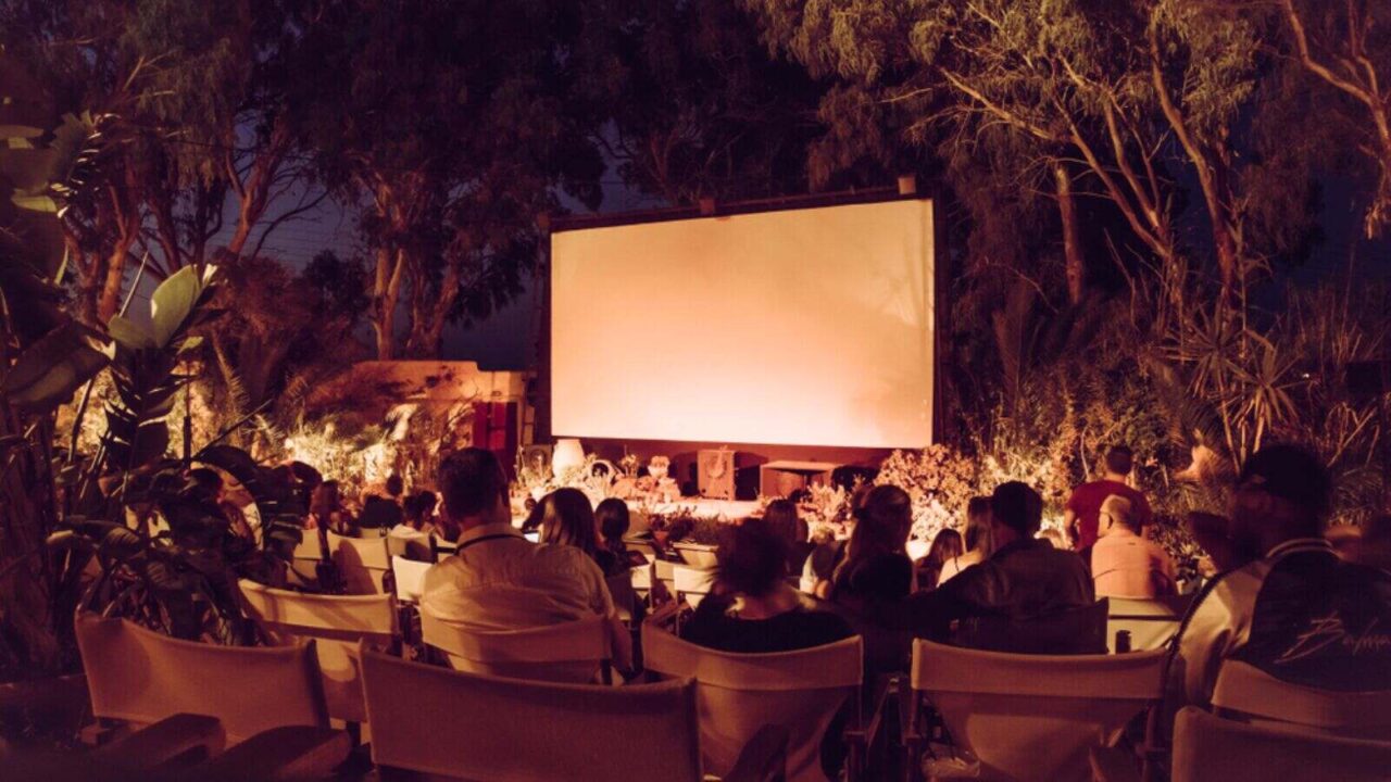 A crowd sitting infront of a screen set up in a garden