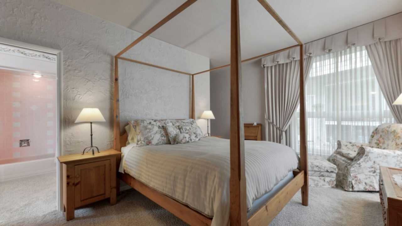 A bedroom interior with wooden canopy bed and floral sofa covers with curtains.