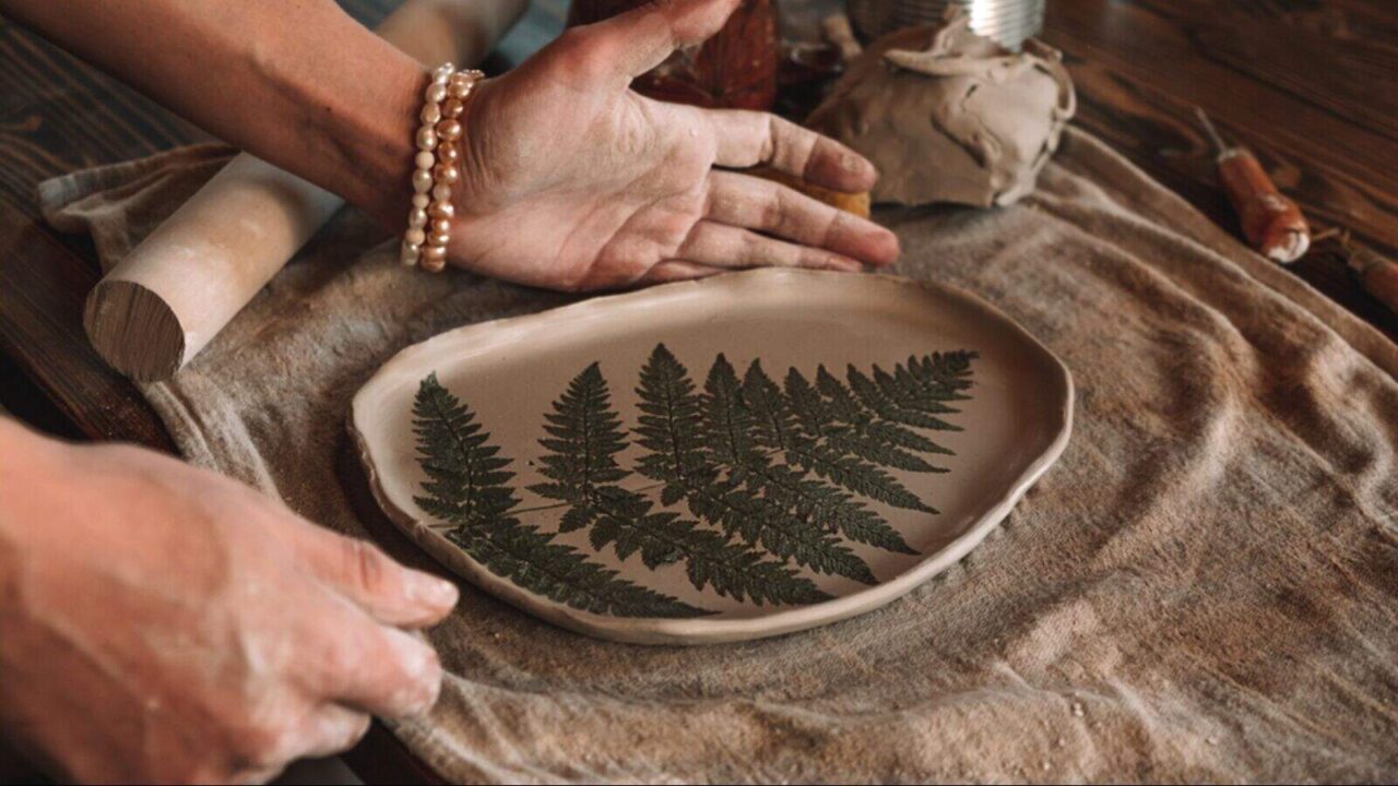 Female sculptor making clay pottery with an imprint of a fern leaf on a clay plate.