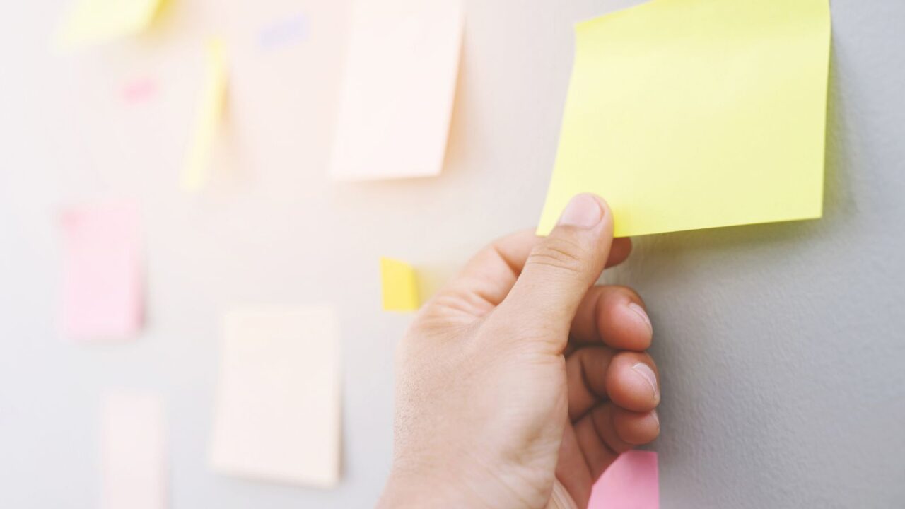 A person pasting a yellow sticky note on a white surface.