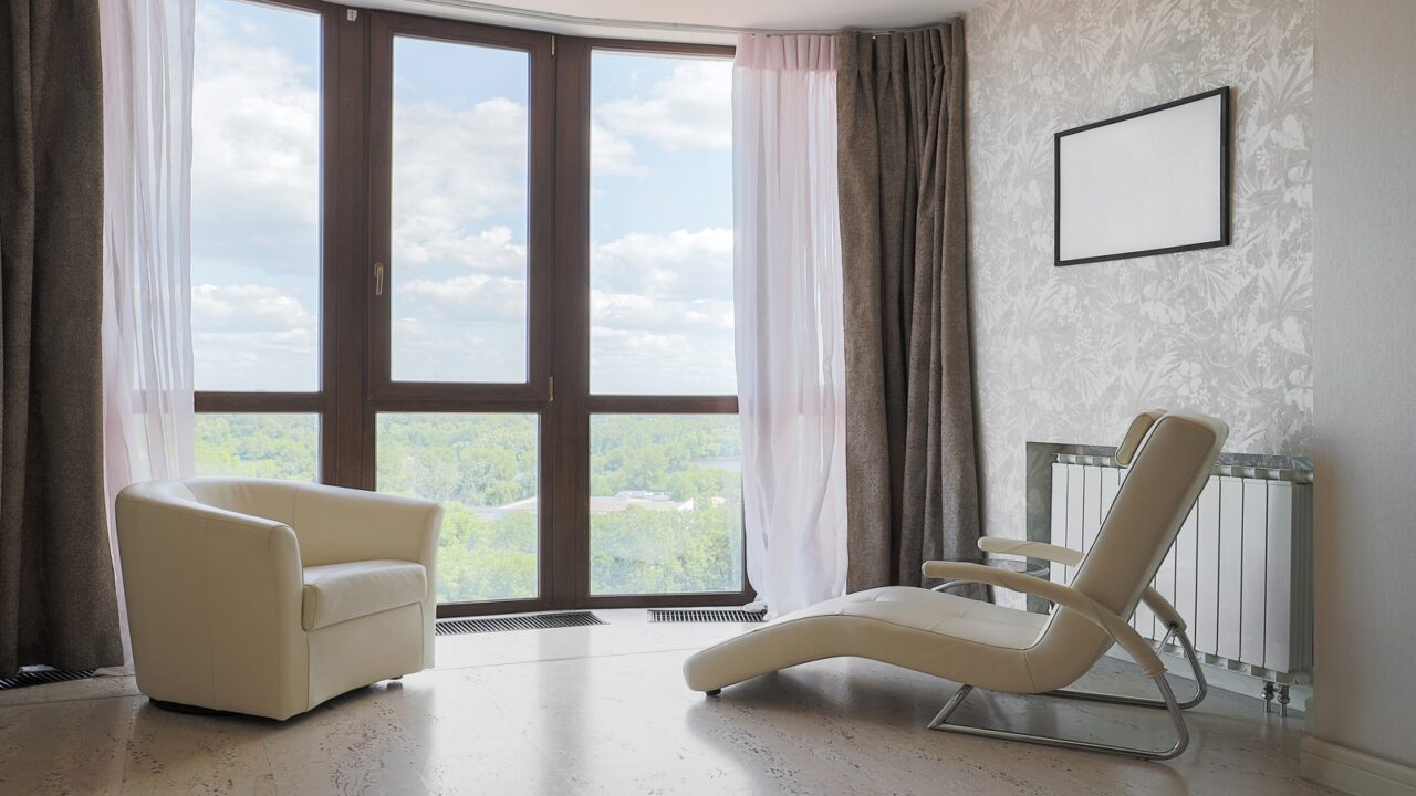 white sofa and recliner in a room with big windows and curtains