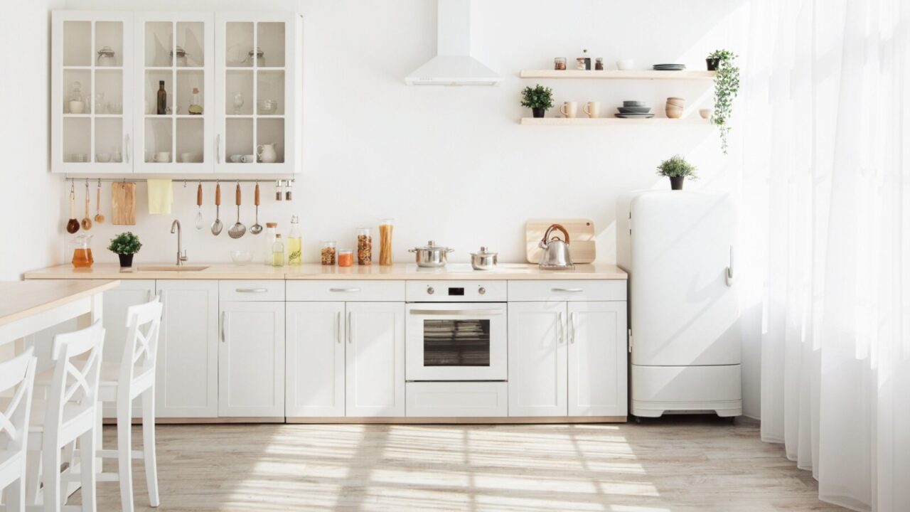 A bright kitchen with white walls and white cabinets, fridge and dining chairs