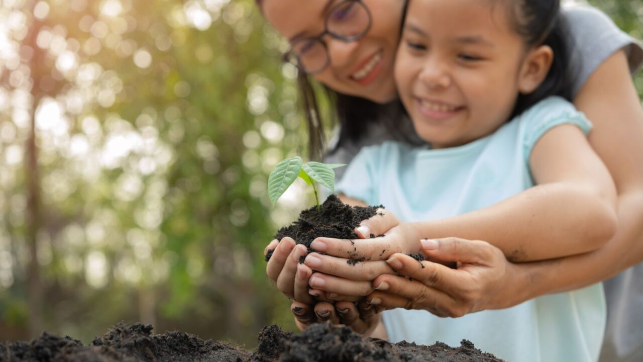 Mom and daughter planting sapling tree.