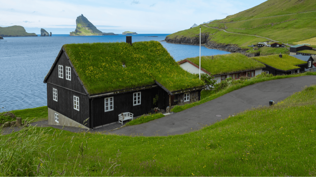 A black house by the sea with grass covered roof in a green valley