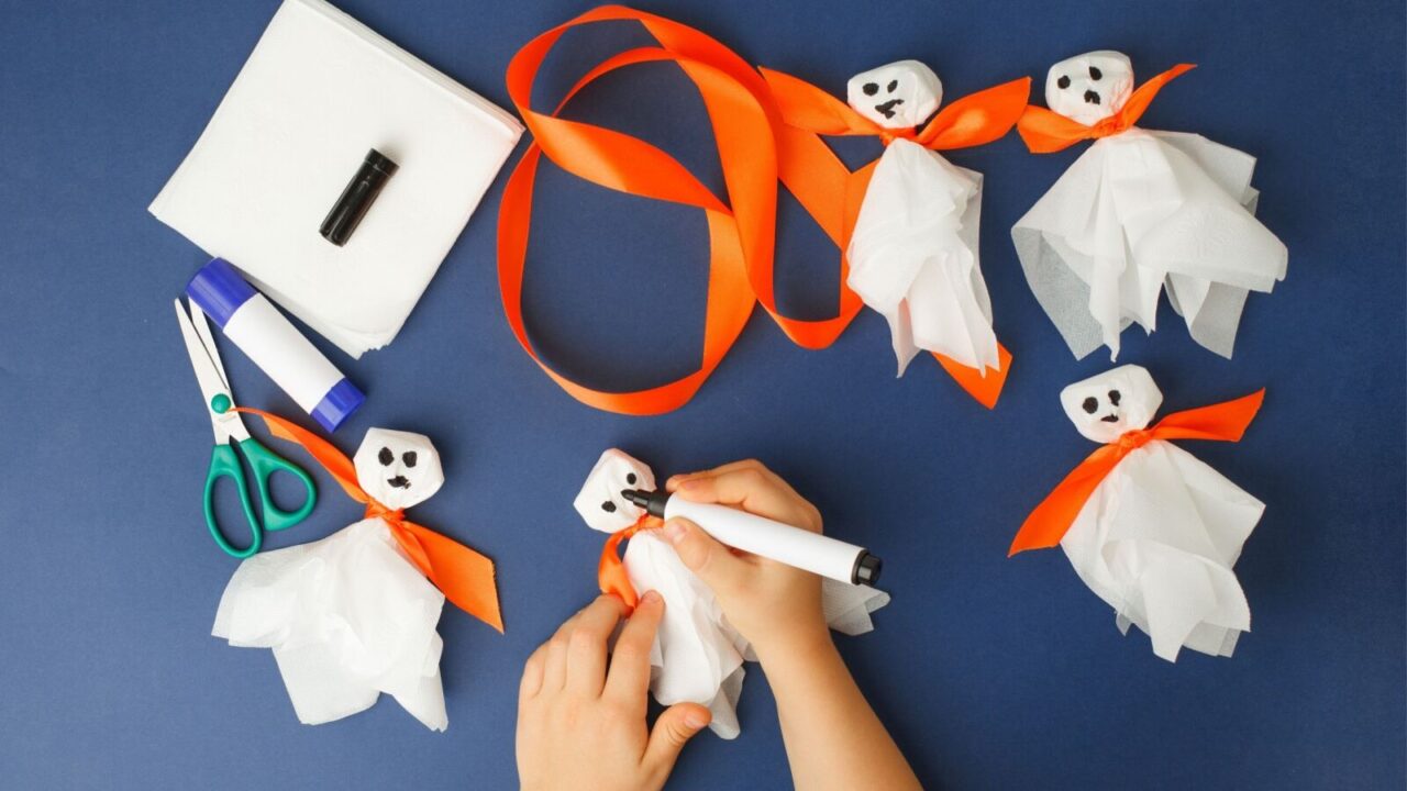 Close up shot of a boy's hand making DIY ghosts with tissue paper and ribbons on a blue table