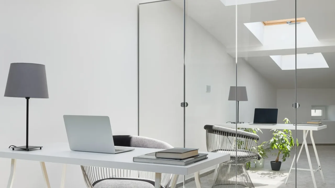 Simple white desk in bright room with ceiling windows, gray carpet flooring and wardrobe with mirrored doors