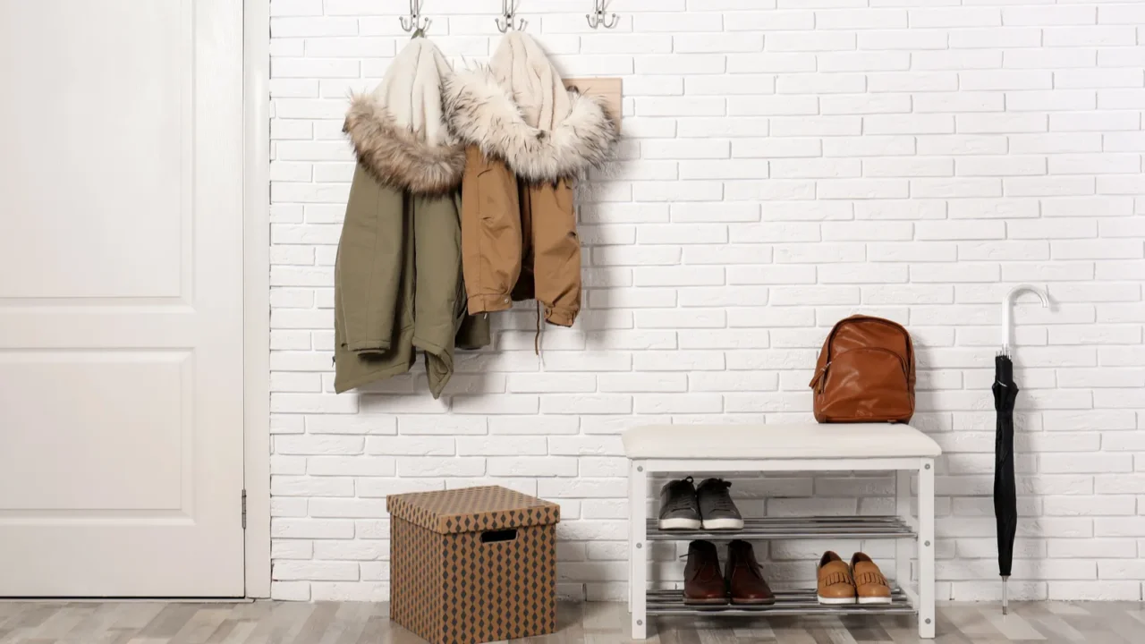 Stylish hallway interior with shoe rack and hanging clothes on brick wall