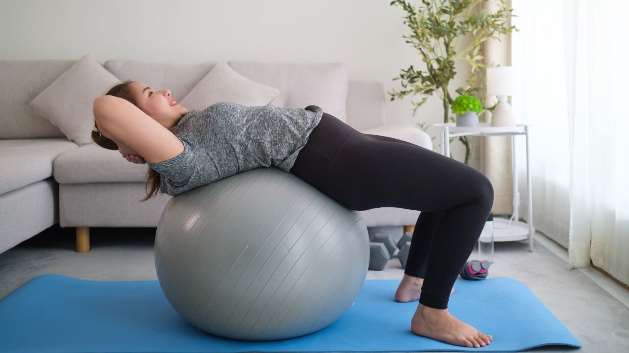 A girl is working out with a stability ball on yoga mat in the living room