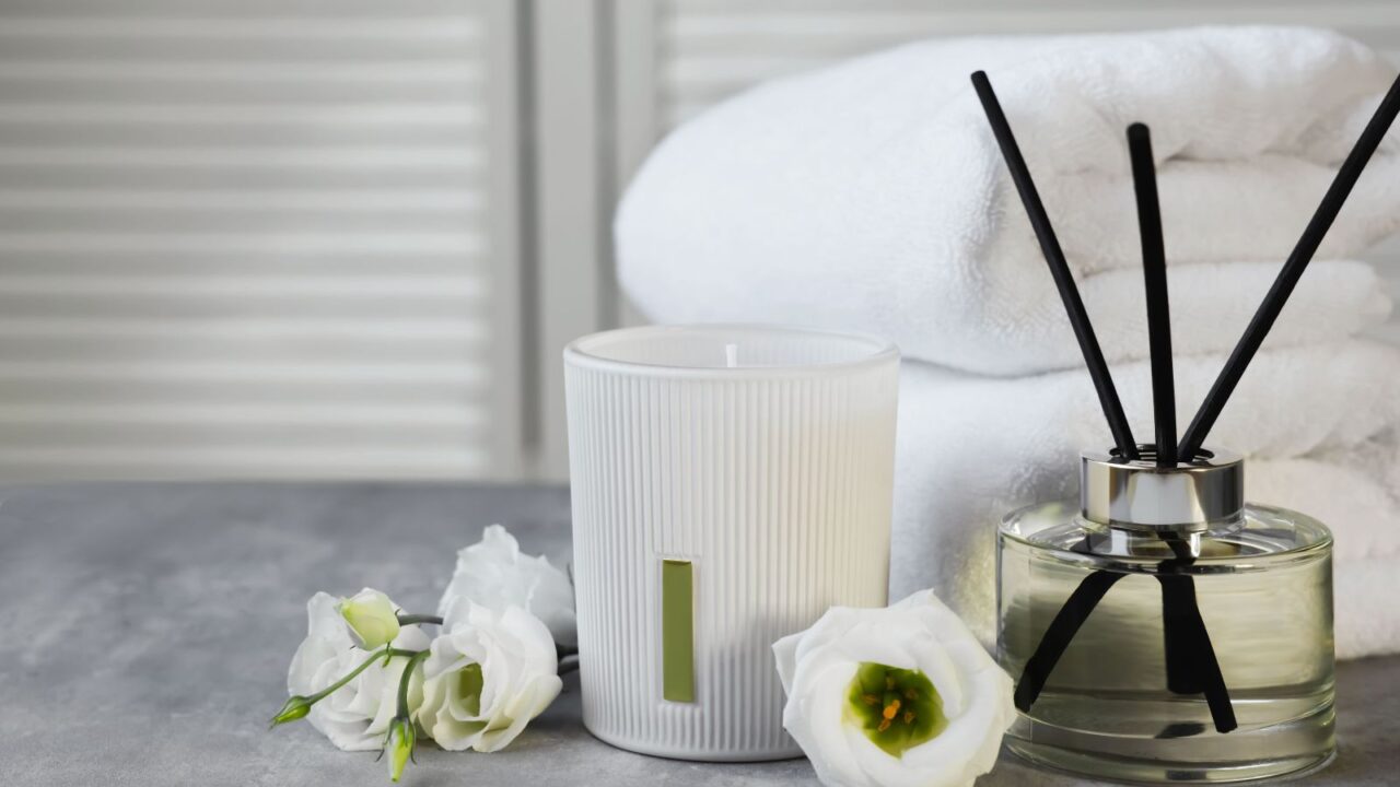 Reed diffuser, scented candle, flowers and folded towels on marble table