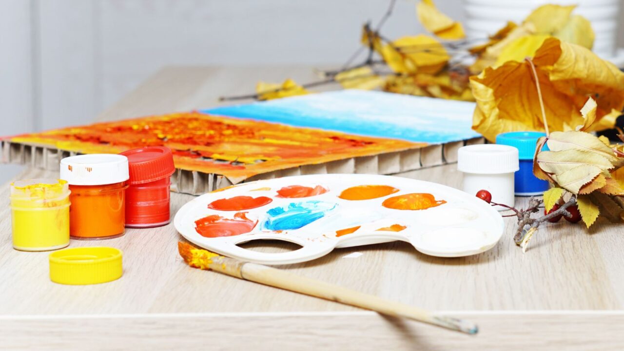 Paints, a palette, yellow leaves of rowan and maple are on the table. It's a children's drawing for the autumn holiday. Fall craft.