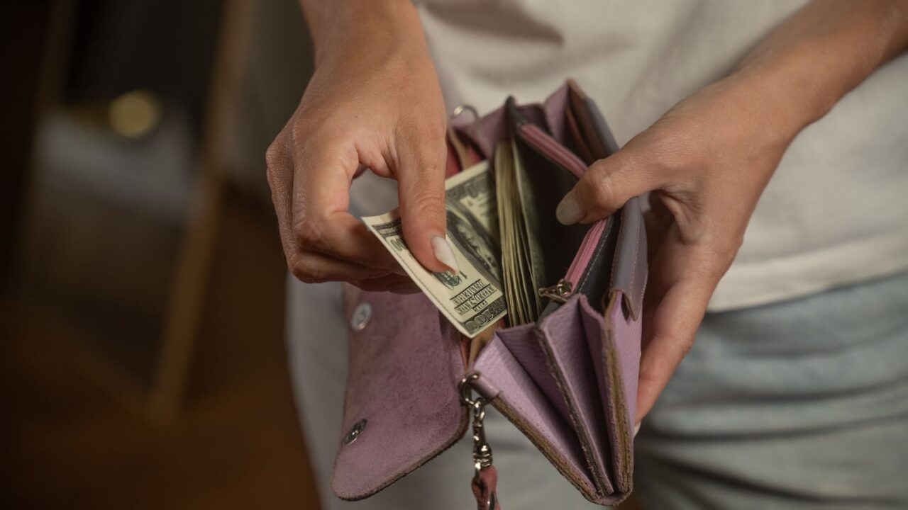 A woman opens a pink wallet, revealing cash.