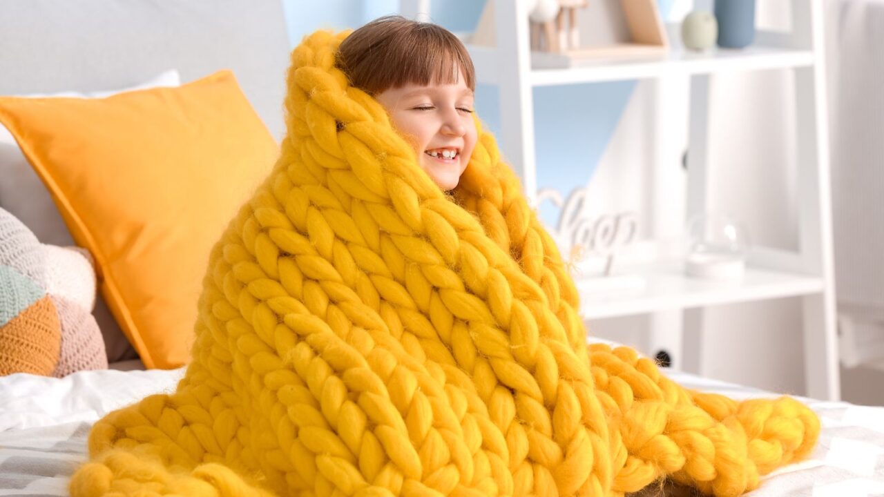 A little girl is feeling happy wrapped in a warm yellow blanket on bed at home