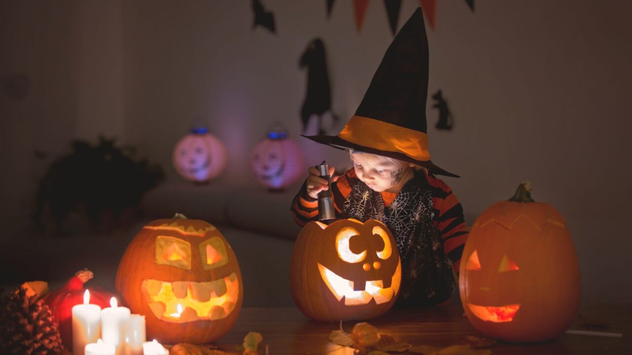 A child is playing with carved pumpkin at home. Halloween decor. Room is decorated with pumpkins and Halloween goodies.