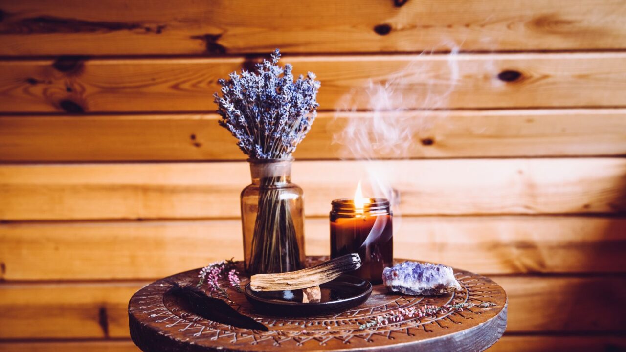 Palo Santo wood known as oily aromatic holy wood sticks smoldering on plate and scented candles on wooden carved wooden table, bohemian style cottage home decor