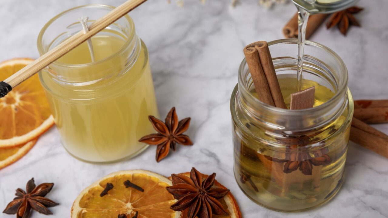 Liquid soy candle wax is poured into a glass jar. decorative element. cinnamon, lemon, cloves, and dried citrus slices for scent