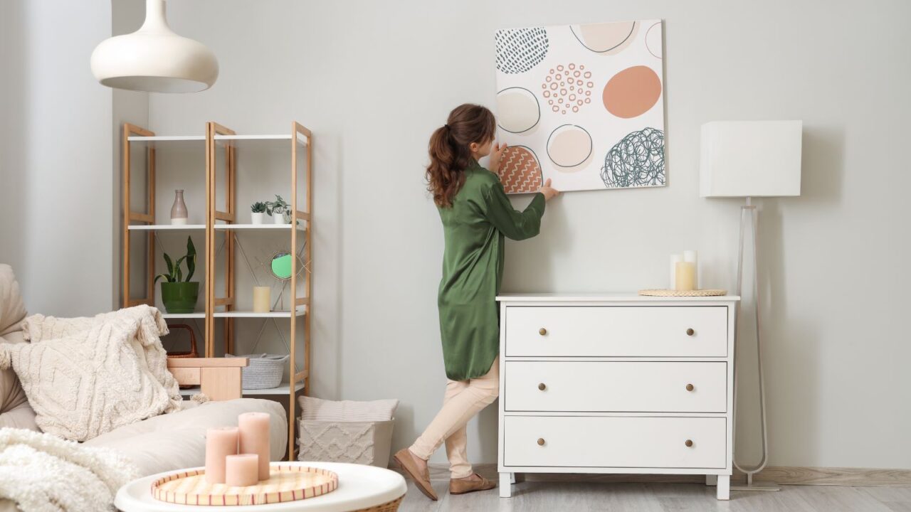 Young woman hanging wall art in a stylish living room.