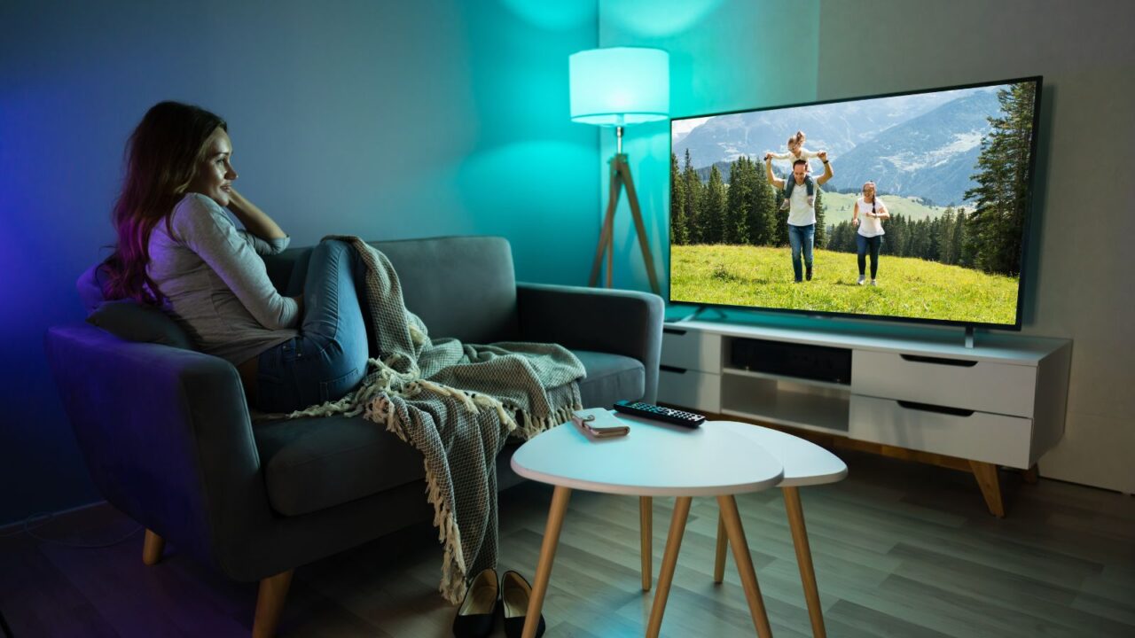 A woman sitting on a sofa with throw blanket watching TV