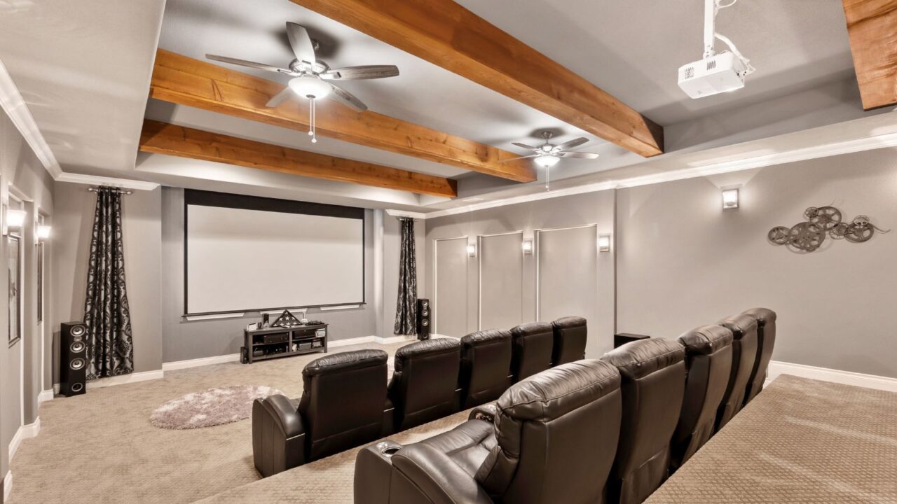 A home theatre interior with cozy seats, a big screen, speakers, fans, and carpeted floor.