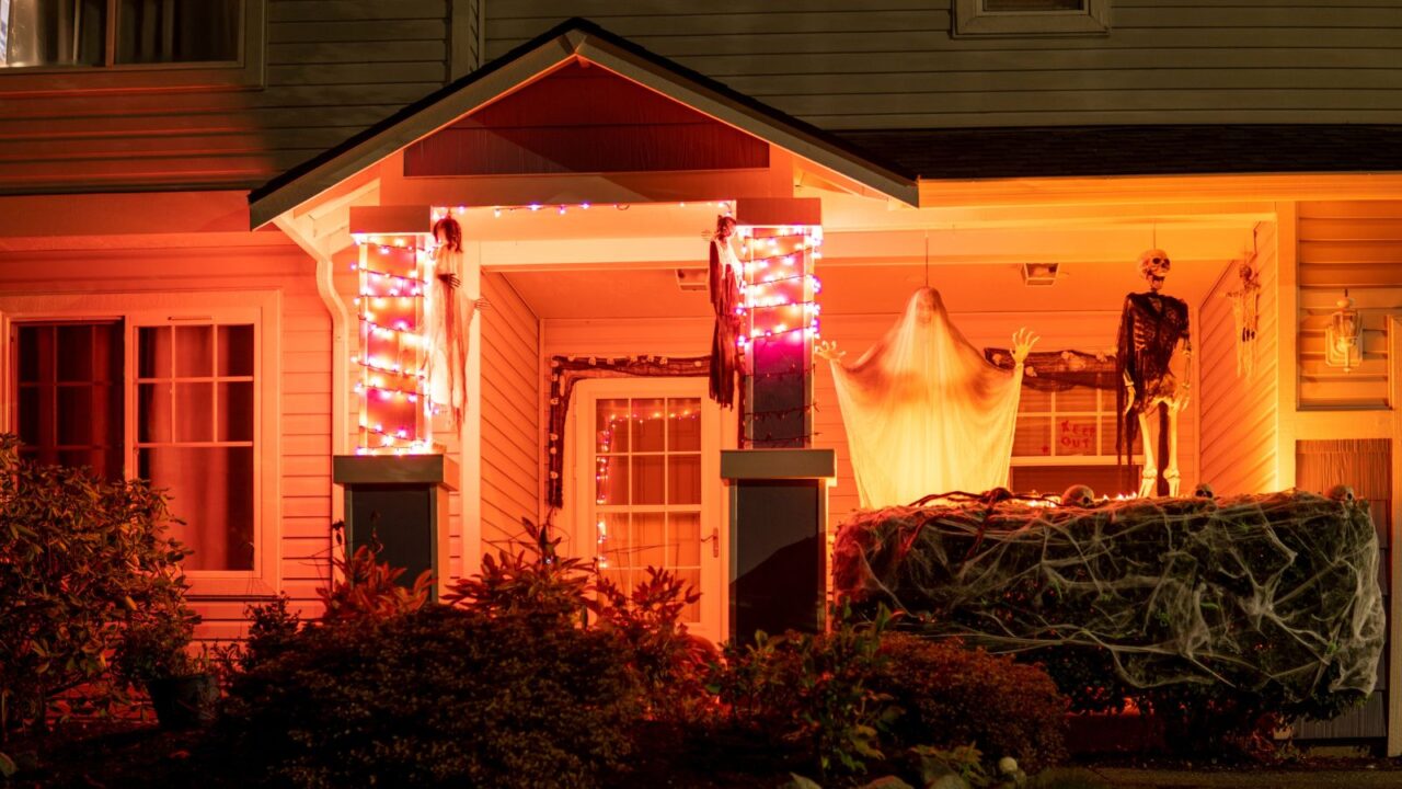 DIY ghost and skeletonhanging on a porch with orange string lights